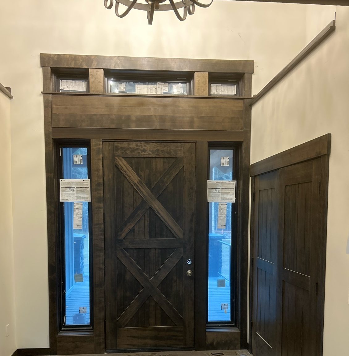 Dark-stained X-brace front door with sidelights and transom windows
